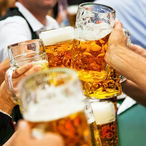 People clink several amber beer steins at a celebration, raising glasses together in a toast.