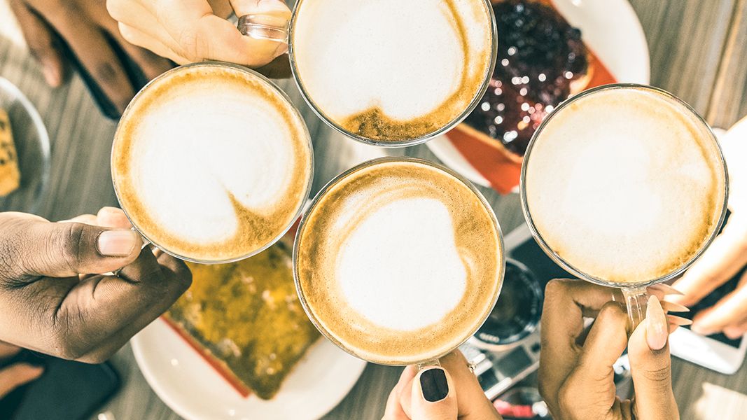 Friends clink coffee mugs over a shared meal, toasting a cozy moment together.