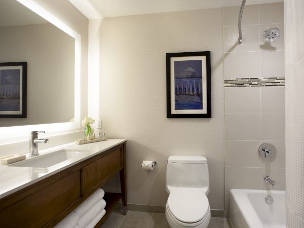 A modern bathroom with a wooden vanity and sink, framed wall art, a toilet, and a tiled shower with a rainfall showerhead.