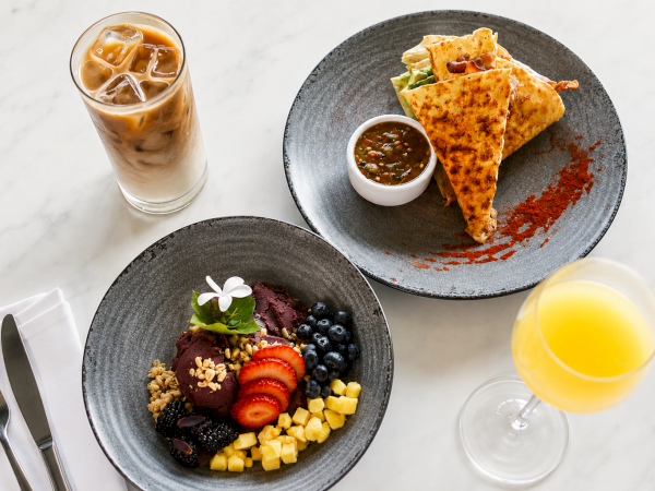 A spread of iced coffee, a tortilla with dipping sauce, and an acai fruit bowl with granola, plus orange juice.