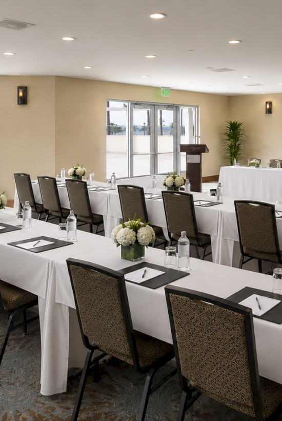 A hotel conference room set with white tablecloths, floral centerpieces, and a sign for The Redondo Beach Hotel.