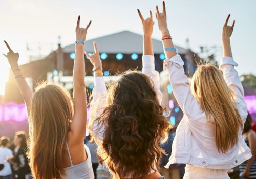 Five people at a concert with their hands in the air, cheering as a stage lights up in the background.
