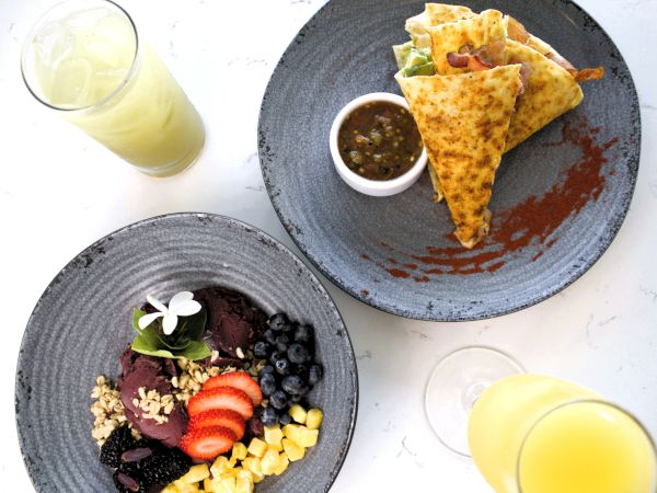 Colorful plates with fruit, granola, and yogurt parfait; quesadillas with salsa or dip; a glass of orange juice; and a light yellow drink.