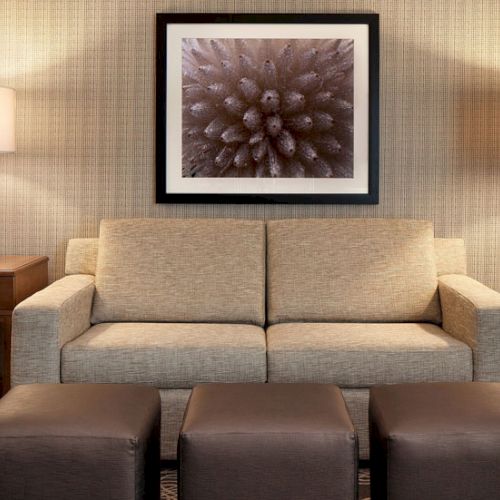 A cozy living room with a beige sofa, two matching lamps, a framed art piece above, and three square ottomans in front, snug and stylish.