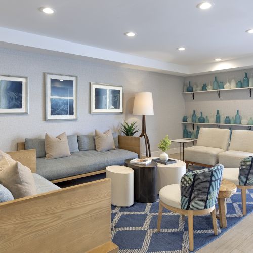 Modern living room with sofa, chairs, coffee tables, framed art, and shelves of blue glass bottles.