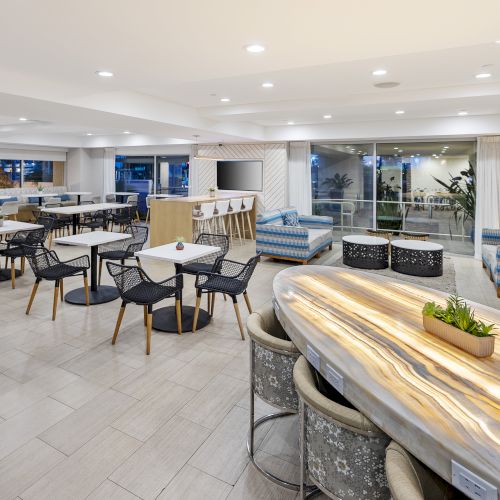 An upscale indoor-outdoor patio lounge with dining tables and chairs, cushioned seating, and a large wooden bar counter.