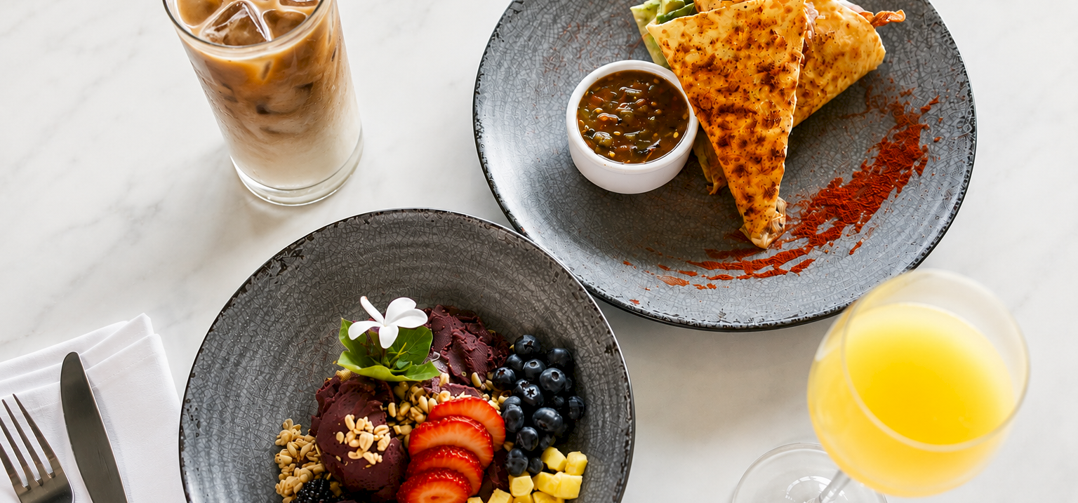 A breakfast spread with iced coffee, soup, cheesy folded nachos, fruit salad, and a glass of orange juice.
