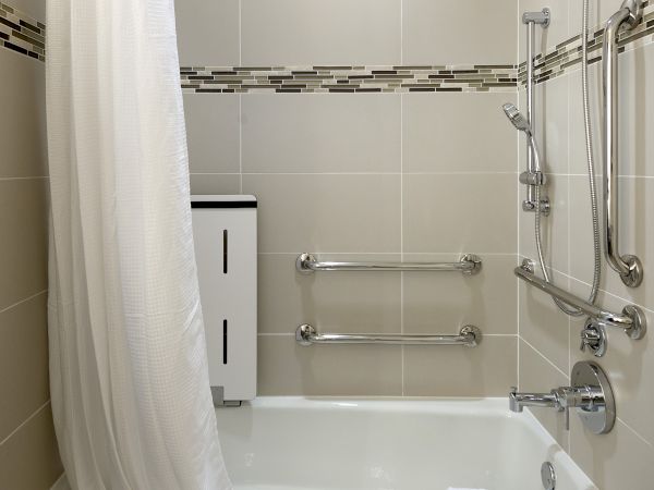 A modern bathroom with a white bathtub, shower curtain, rainfall shower head, chrome grab bars, and folded towels.