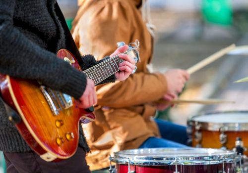 Guitar and drums being played in a band scene, close-up of hands on strings and sticks, outdoors, casual jam session.