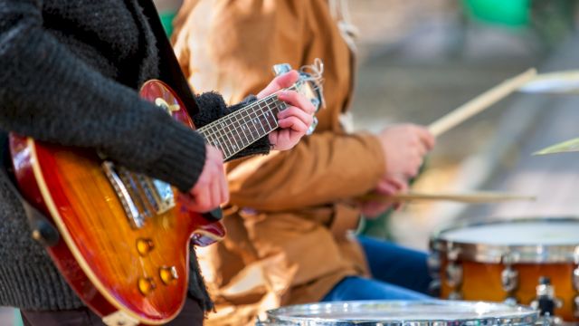 Guitar and drums being played in a band scene, close-up of hands on strings and sticks, outdoors, casual jam session.