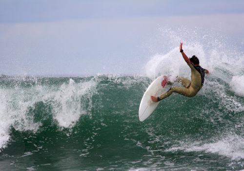 A surfer executes an arcing turn on a hollow green wave, spray flying as they ride a white shortboard. End.