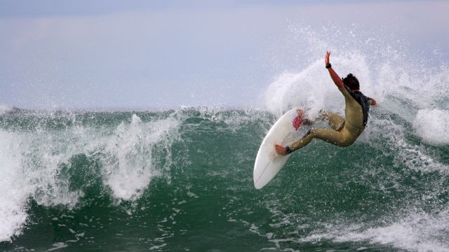 A surfer executes an arcing turn on a hollow green wave, spray flying as they ride a white shortboard. End.