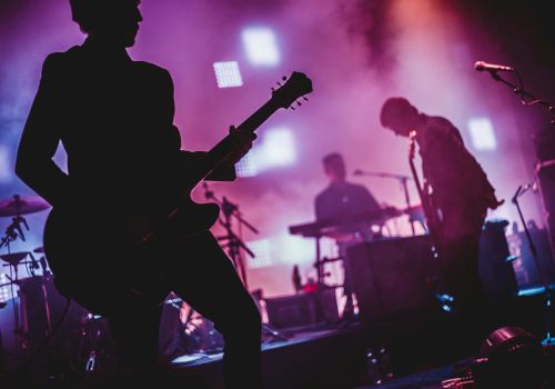 A rock band performing on stage with silhouetted guitarists, drummer, and vibrant purple lighting.