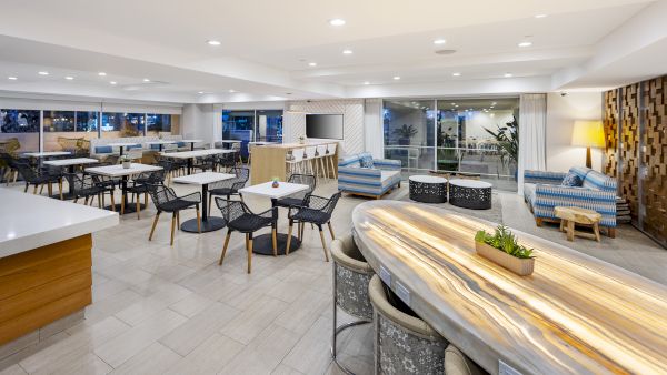 Bright modern patio lounge with outdoor-style tables and chairs, built-in seating, and a TV near large sliding windows.