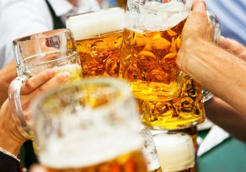 People clink several amber beer steins at a celebration, raising glasses together in a toast.