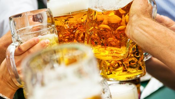 People clink several amber beer steins at a celebration, raising glasses together in a toast.